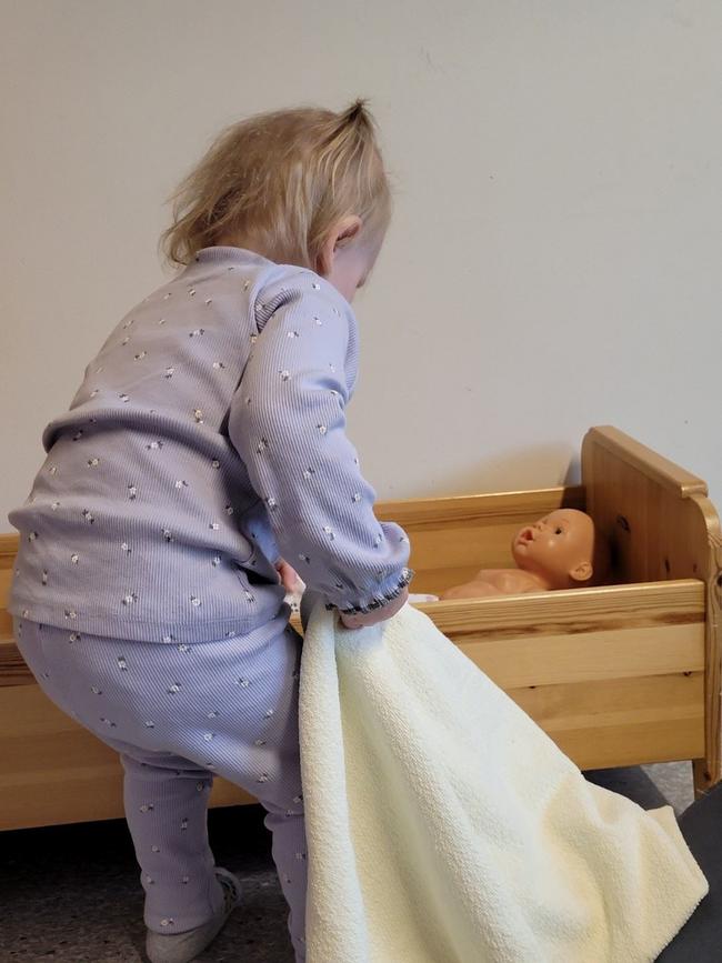 liten jente leker med dukke, teppe og dukkeseng