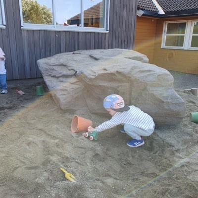 et barn leker i en sanddunge foran en kjempestor stein
