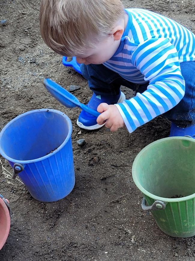 et barn med stripete genser leker med blå bøtte og spade i sanda