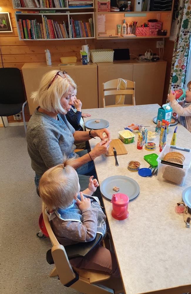 en voksen og tre barn sitter rundt bord og spiser brød og pålegg