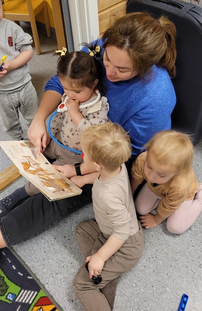 Et voksen leser i bok, tre barn sitter rundt og ser i boka